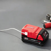 Red and black Milwaukee battery pack on a gray surface with tools in the background