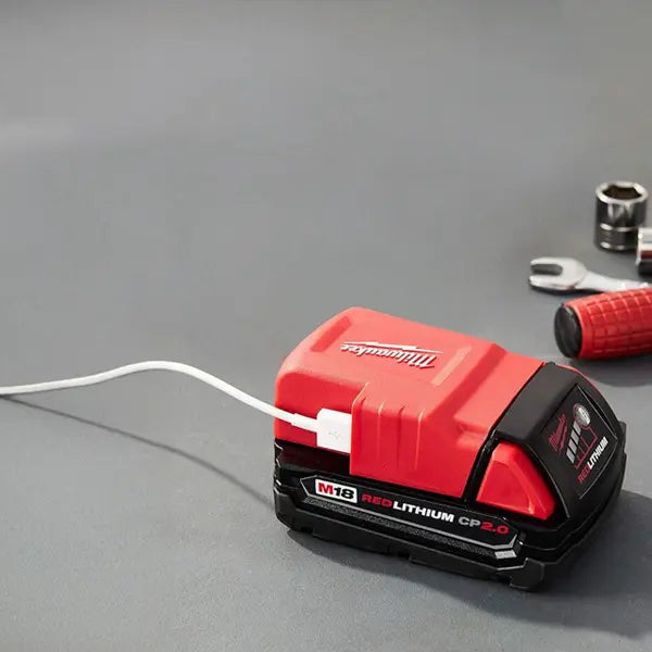 Red and black Milwaukee battery pack on a gray surface with tools in the background