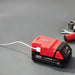 Red and black Milwaukee battery pack on a gray surface with tools in the background