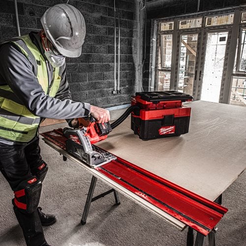 Person using a circular saw on a workbench with a Milwaukee toolbox in a construction setting.