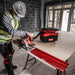 Person using a circular saw on a workbench with a Milwaukee toolbox in a construction setting.