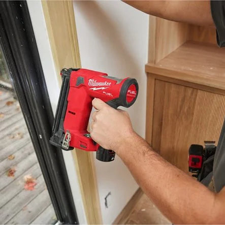 Person using a Milwaukee FUEL nailer on a wooden shelf.
