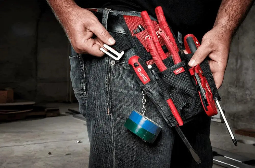 Person holding a milwaukee tool belt with various hand tools in an industrial setting