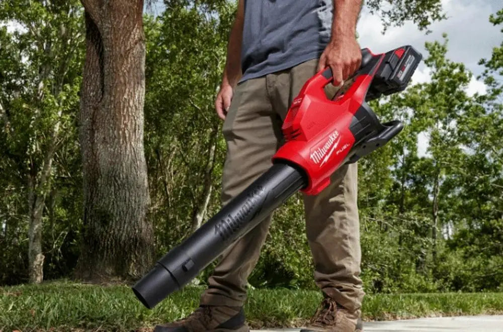 Person holding a milwaukee fuel leaf blower in an outdoor setting with trees and grass.
