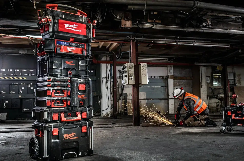 Stack of Milwaukee packout toolboxes in a warehouse with a worker in the background.
